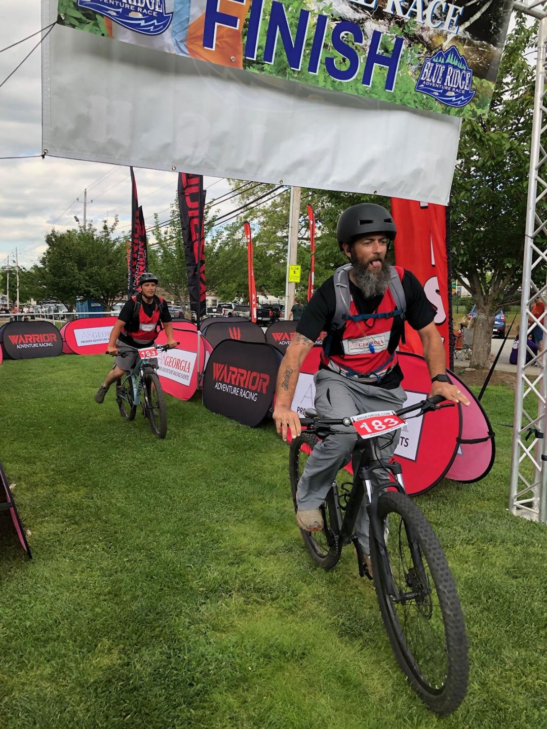 Photo of two members of the Appalachian Circuit Veterans Treatment Court as they ride their mountain bikes across the finish line at the Blue Ridge Adventure Race.