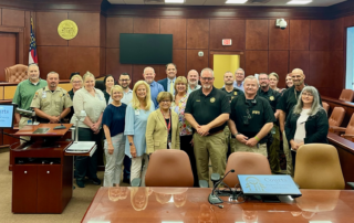 Group photo of 20 officials and constituents standing inside a courtroom for a group photo.
